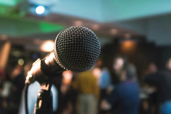 A close-up of a microphone with a blurred audience in the background, possibly at an event or performance.