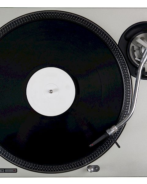 The image shows a vinyl record on a turntable, including a tonearm and stylus, used for playing music from records.