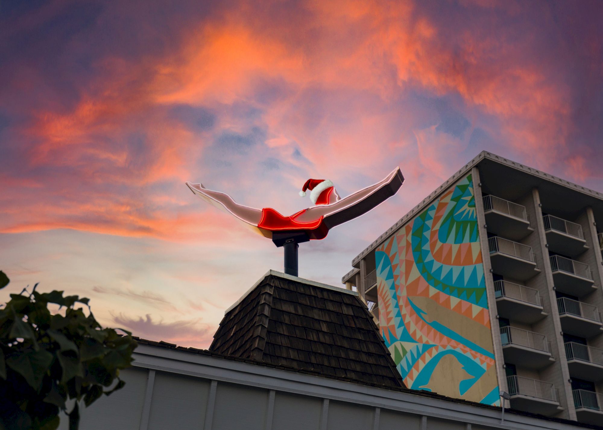 A sculpture of a diving female figure on a building with a colorful mural and sunset sky in the background, creating a striking visual contrast.