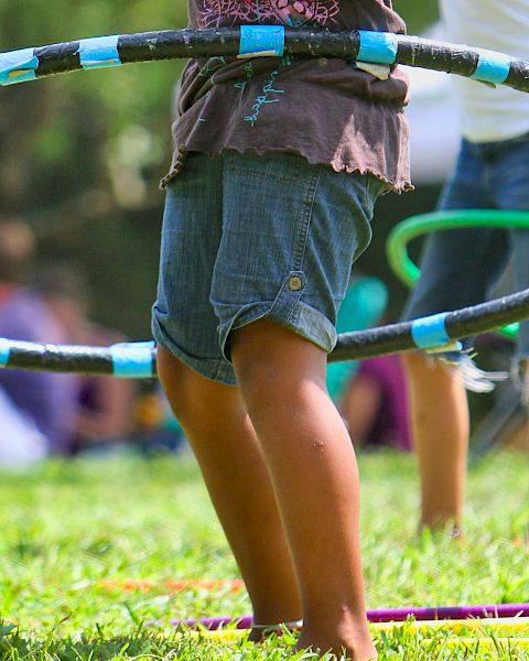 Children are playing with hula hoops on a grassy field, engaging in outdoor fun and enjoying the sunny day.