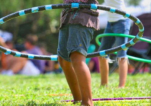 Children are playing with hula hoops on a grassy field, engaging in outdoor fun and enjoying the sunny day.