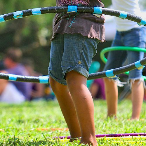 Children are playing with hula hoops on a grassy field, engaging in outdoor fun and enjoying the sunny day.