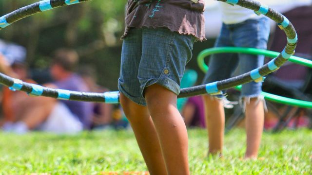 Children are playing with hula hoops on a grassy field, engaging in outdoor fun and enjoying the sunny day.