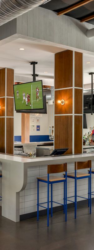 The image shows a modern bar and dining area with a central counter surrounded by stools, flat-screen TVs, wooden tables, and chairs, ending the sentence.