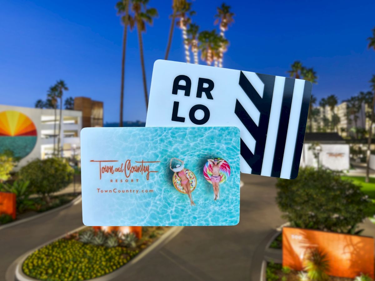 Two gift cards overlay a vibrant outdoor scene with palm trees and a colorful sunset mural.