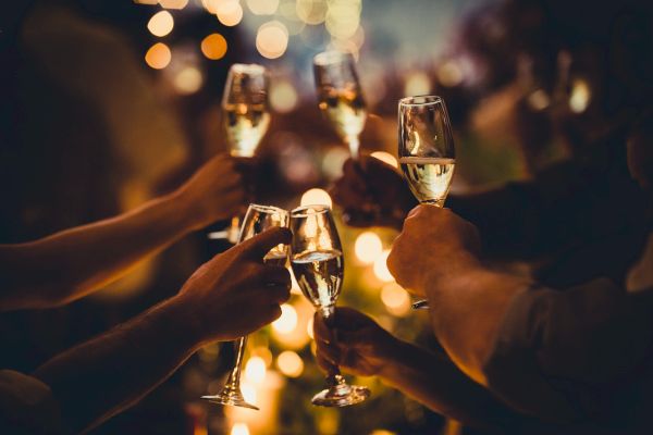 People are raising glasses of champagne in a toast at a festive gathering, with blurred lights in the background.