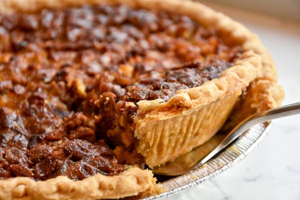 The image shows a close-up of a pecan pie with a slice being cut out, revealing a rich, nutty filling.