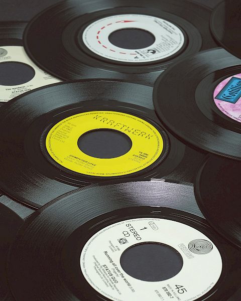 The image shows a collection of vinyl records scattered on a flat surface, each with different colored labels and designs, with black edges.