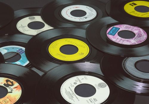 The image shows a collection of vinyl records scattered on a flat surface, each with different colored labels and designs, with black edges.