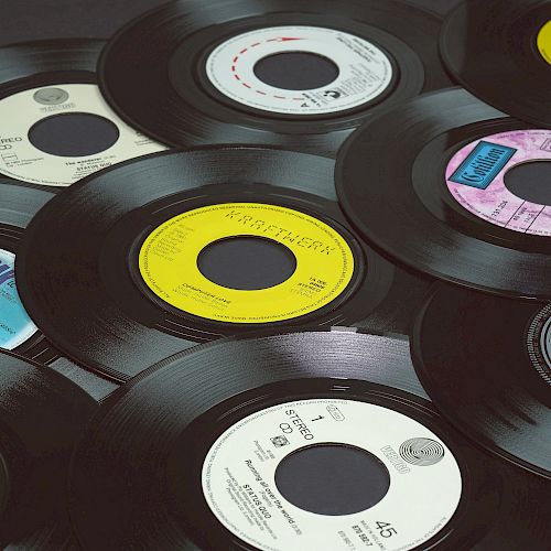 The image shows a collection of vinyl records scattered on a flat surface, each with different colored labels and designs, with black edges.