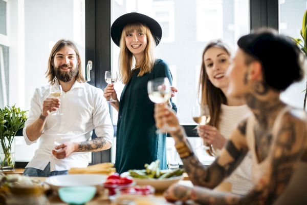 A group of four people enjoying a casual gathering, smiling and holding glasses, in a bright, modern room with a table of food.