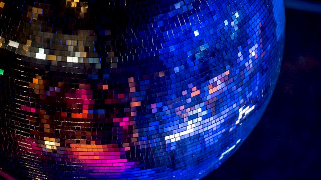 The image shows a close-up of a shiny disco ball reflecting colorful lights in a dark environment.