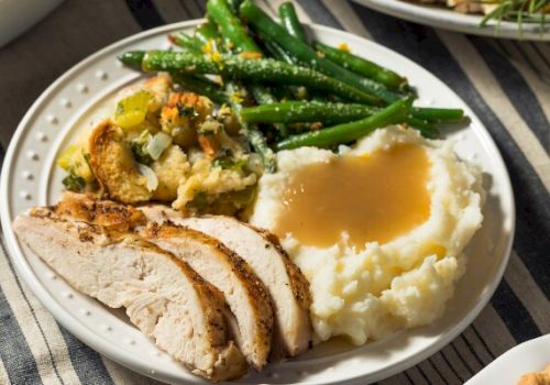 A plate with sliced turkey, mashed potatoes with gravy, green beans, and stuffing.