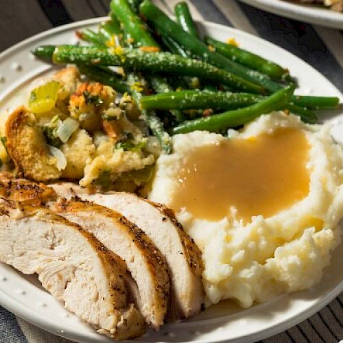 A plate with sliced turkey, mashed potatoes with gravy, green beans, and stuffing.