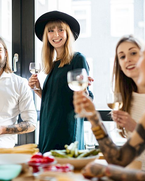 A group of four people enjoying a meal together, holding glasses and smiling around a table with food and drinks.