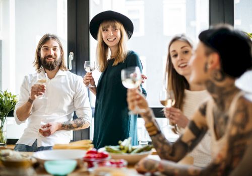 A group of four people enjoying a meal together, holding glasses and smiling around a table with food and drinks.