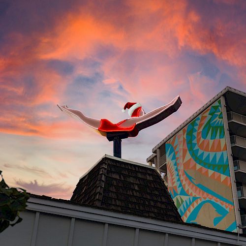 A rooftop sculpture of a swimsuit-clad diver against a colorful sunset sky, with a building showing a geometric mural in the background.