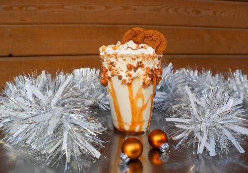 A caramel milkshake topped with whipped cream, cookies, and caramel drizzle, surrounded by silver tinsel and small gold ornaments.