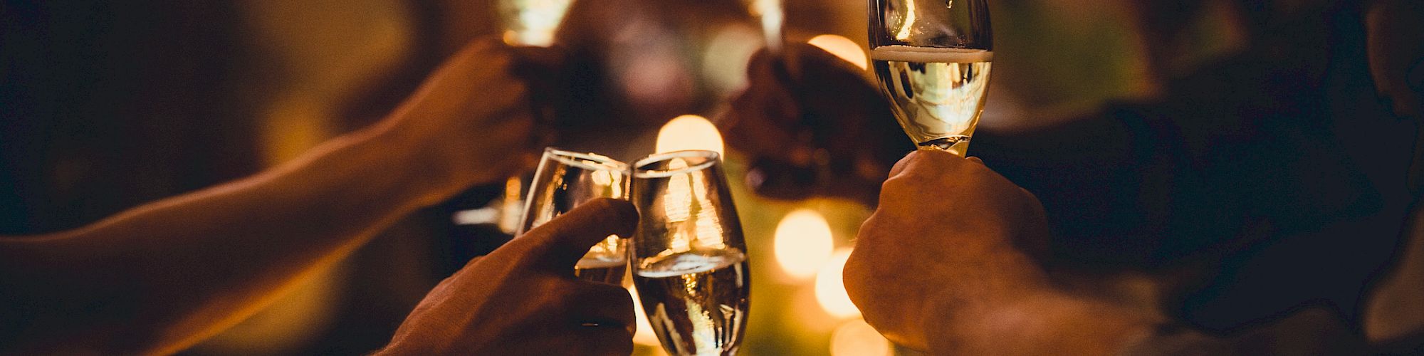 People raising champagne glasses in a celebratory toast, with warm lighting and out-of-focus background creating a festive atmosphere.