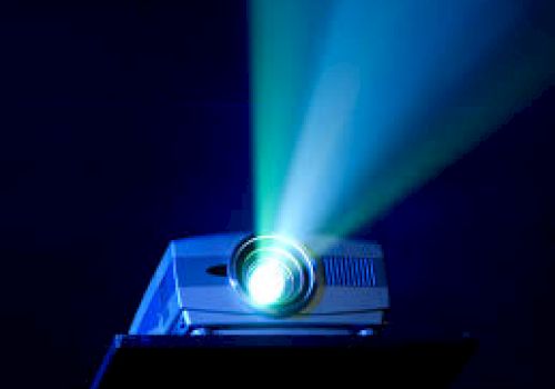 The image shows a projector emitting bright blue and green light beams in a dark setting.