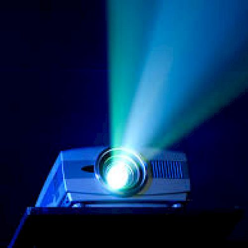 The image shows a projector emitting bright blue and green light beams in a dark setting.