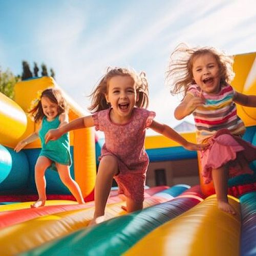 Three children are joyfully running on a colorful inflatable bounce house, with smiles and sunlight enhancing their playful moment.