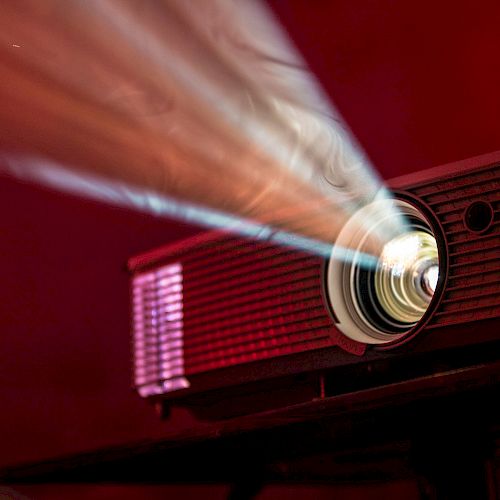 An image of a projector casting a beam of light, set against a red background, creating a cinematic and dramatic effect.