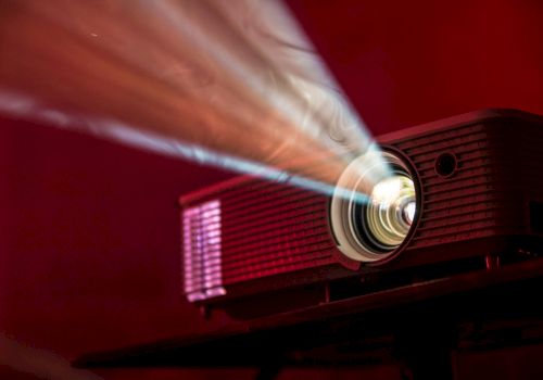 An image of a projector casting a beam of light, set against a red background, creating a cinematic and dramatic effect.