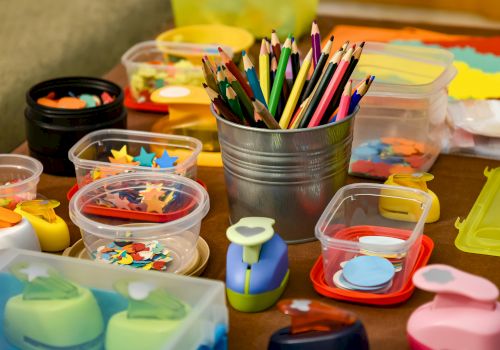 The image shows a collection of colored pencils, shaped punches, and containers filled with various colorful paper cutouts for crafts.