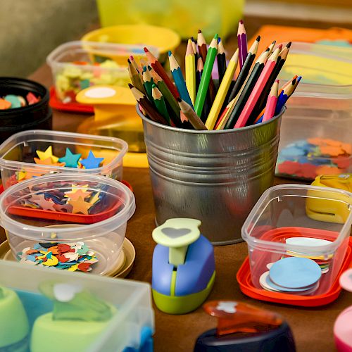 The image shows a collection of colored pencils, shaped punches, and containers filled with various colorful paper cutouts for crafts.