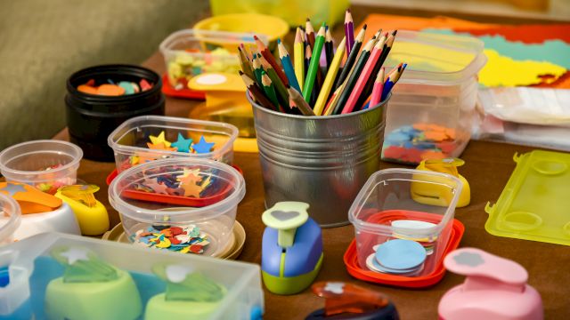 The image shows a collection of colored pencils, shaped punches, and containers filled with various colorful paper cutouts for crafts.